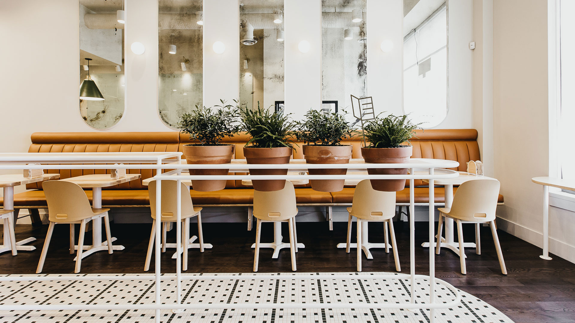Gray Olive Cafe interior design by Cutler, showing tables, chairs, plants, mirrors, and patterned floor tiles