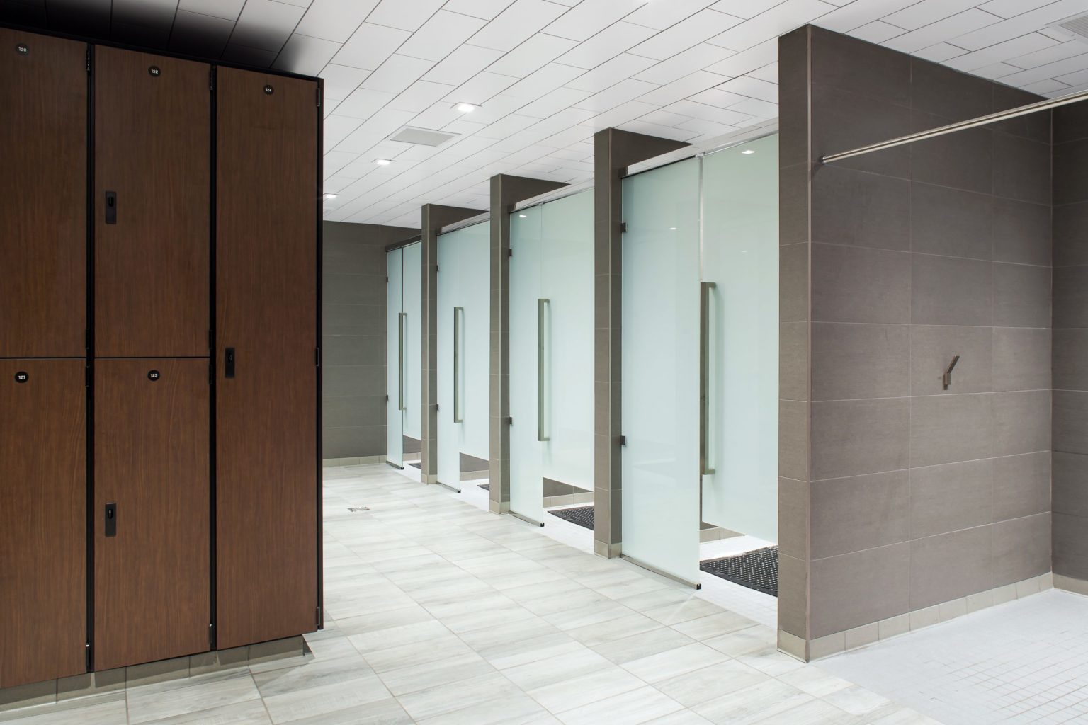 Gym change room with private glass shower stalls, large-format tile and wall-hung lockers designed by Cutler