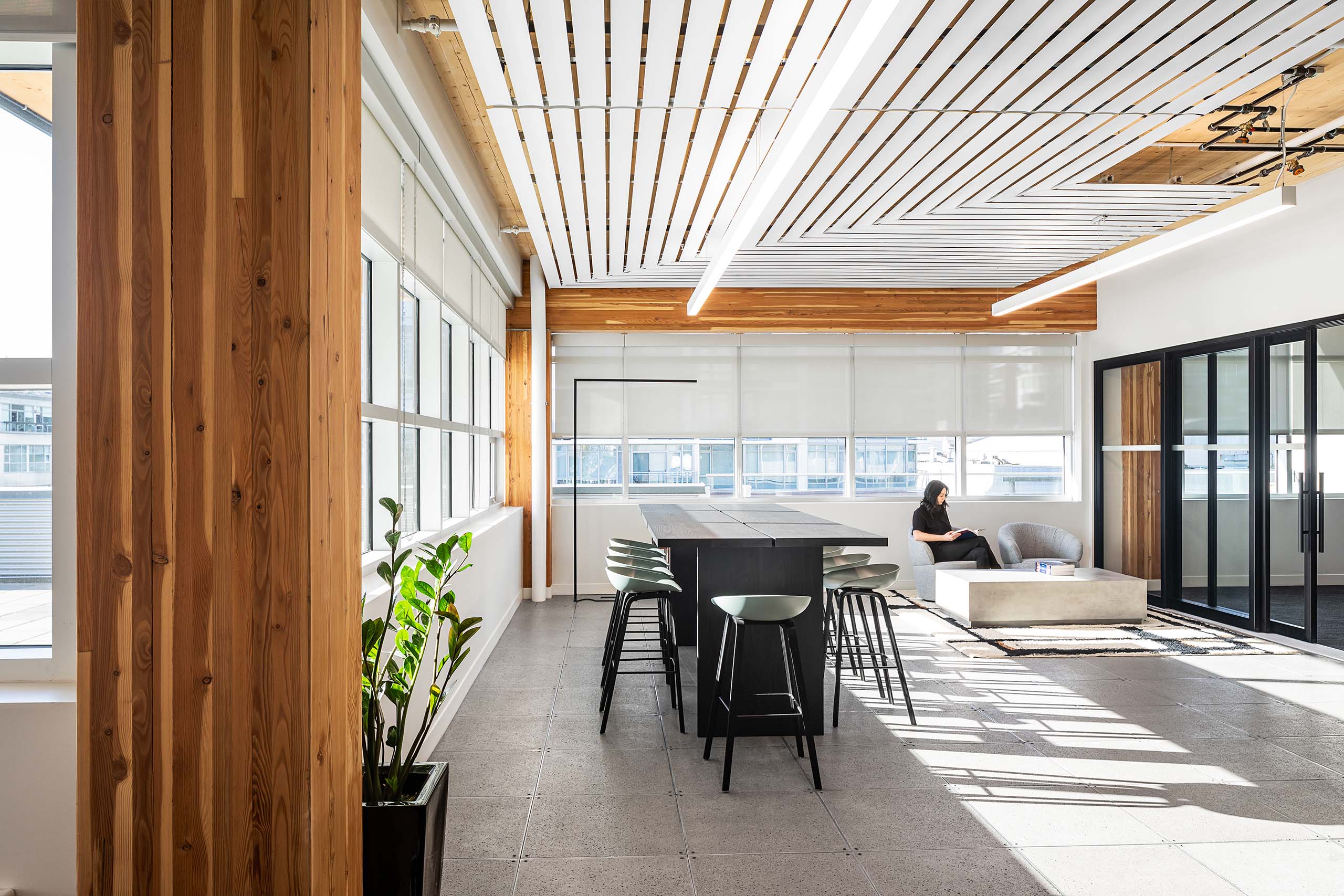 Wylie Crump office and workspace interior design showing lounge area, bright walls, windows with light streaming in, and a person reading a book in the lounge area