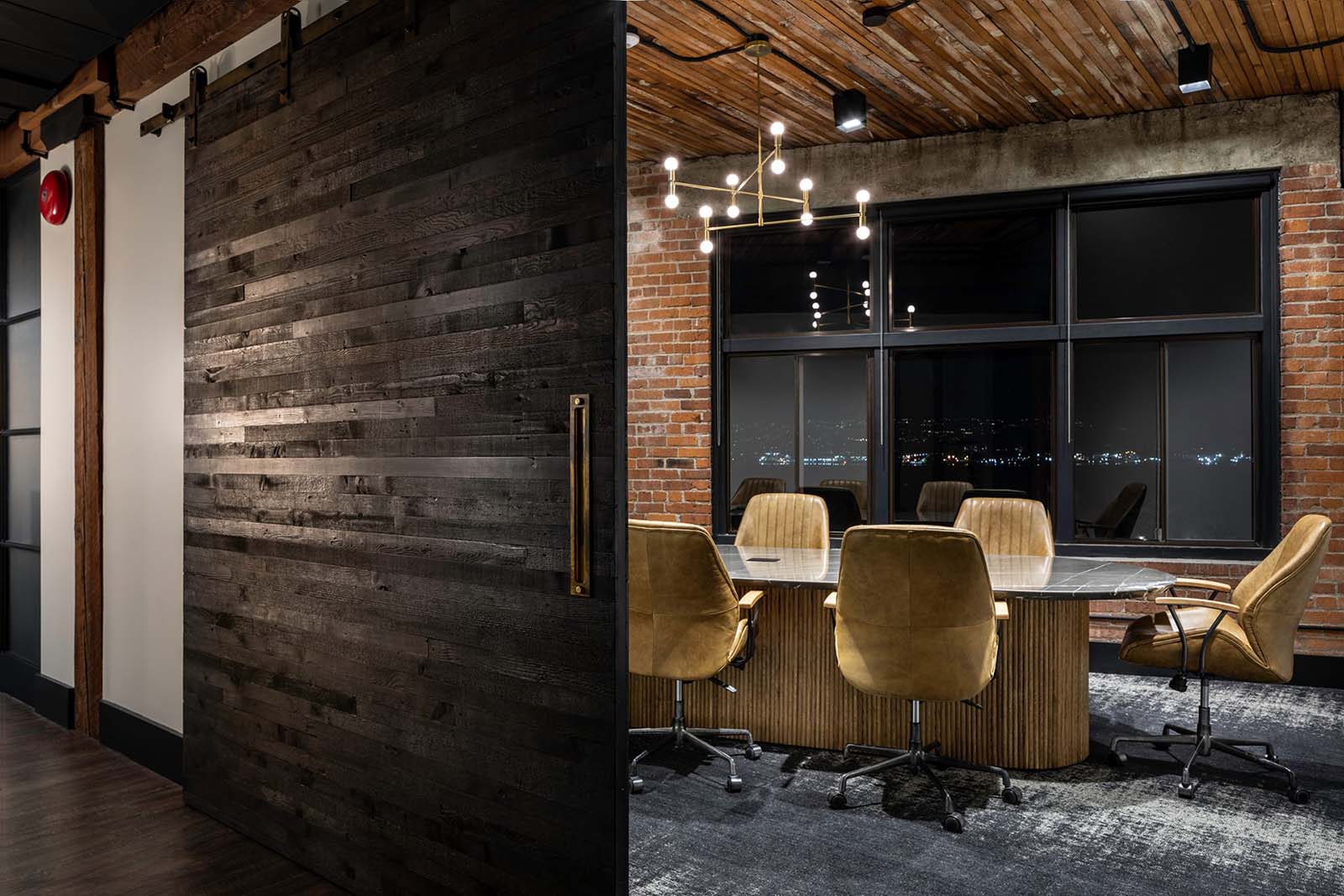 Workspace interior showing sliding wood panel wall, conference room and chairs, and big window looking at Vancouver night sky. Key Marketing office design by Cutler.